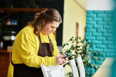 Parlak bir kafede, Down sendromlu güçlü genç bir kadın telefonunu kullanırken rahatlıyor..