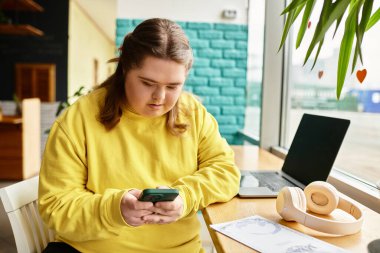 Down sendromlu kendine güvenen genç bir kadın parlak bir kafede oturuyor ve akıllı telefonuyla meşgul oluyor..