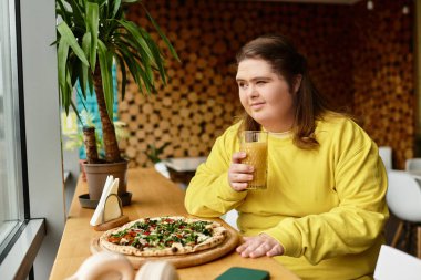 Kendine güvenen genç bir kadın bir kafede pizza ve içkiden zevk alır ve güçlü ruhunu gösterir..
