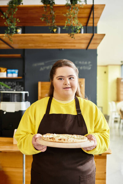 In a lively cafe, a young woman with Down syndrome proudly displays a fresh pizza.