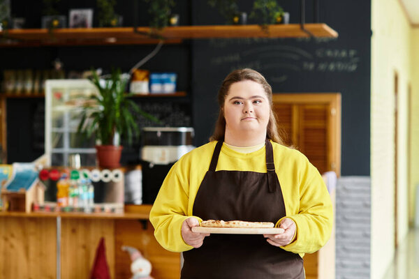 A young woman with Down syndrome proudly presents baked goods on a tray in a cafe.