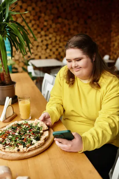 Down sendromlu genç bir kadın açık bir kafede pizza ve telefonu seviyor..