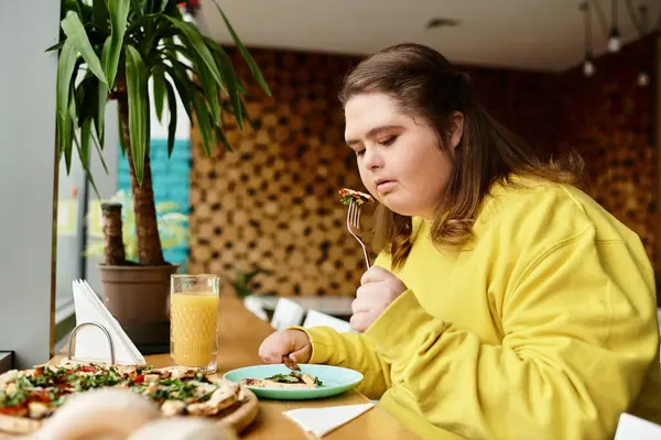 Down sendromlu genç bir kadın yemeğinin tadını çıkarıyor ve bir kafe ortamında kendine güven yayıyor..