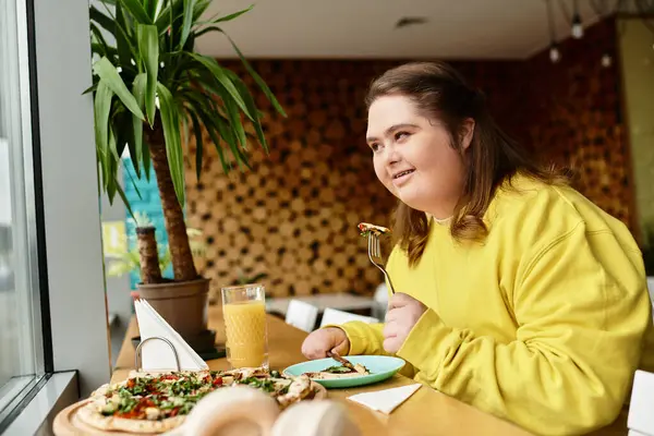 Down sendromlu genç bir kadın sıcak bir kafede yemeğinin tadını çıkarırken gülümsüyor..