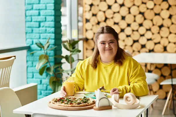 Down sendromlu kendine güvenen genç bir kadın bir kafe masasında oturup yemek ve içeceğin tadını çıkarıyor..