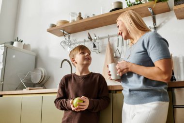 Modern bir mutfakta, bir anne oğluna yeşil elmadan zevk alırken gülümser..