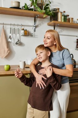 Bir anne, sıcak ve modern bir mutfakta neşeli bir anı paylaşarak oğluna sarılır..