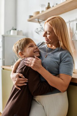 Anne ve oğul, modern mutfak alanlarında sevgi ve sıcaklık saçan samimi bir kucaklaşmayı paylaşıyor..
