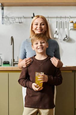 Bir kadın ve oğlu modern bir mutfakta birlikte duruyorlar, içkilerini paylaşırken sıcacık gülümsüyorlar..