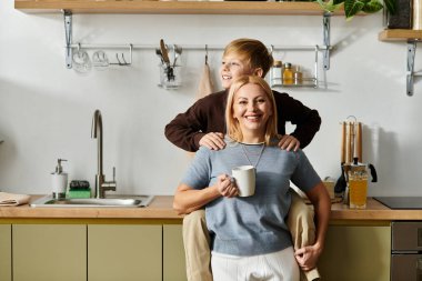 Neşeli bir anne sıcak bir içki tutar, oğlu şakacı bir şekilde arkasında tünemiştir..