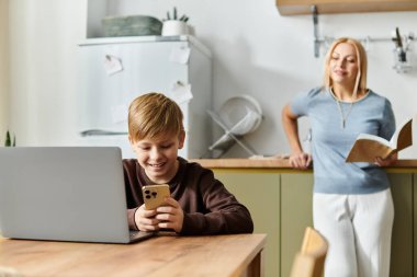 Bir anne, oğlunun rahat bir mutfak masasında akıllı telefonuyla meşgul olmasını gülümseyerek izler..