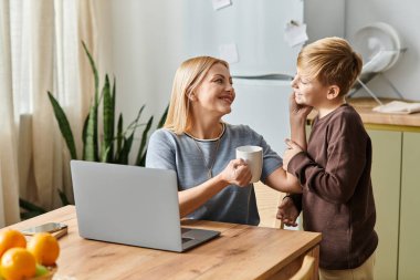 Bir anne güneşli mutfak masasında çay içerken oğluyla keyifli bir etkileşimden hoşlanır..