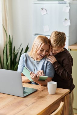Bir anne ve oğlu güler ve öğleden sonra güneşli bir mutfak masasında birlikte yaratırlar..