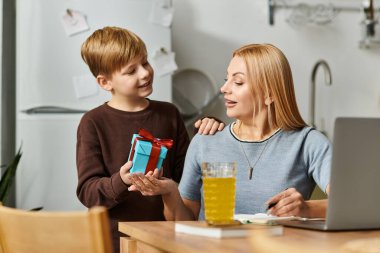 Bir çocuk, sevgi dolu sıcak bir mutfak ortamında annesine renkli bir hediye sunar..