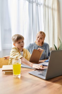 Bir kadın, güneşli, tahta bir masada, birlikte geçirdikleri zamanın keyfini çıkarırken, oğluna ödevlerinde yardım eder..
