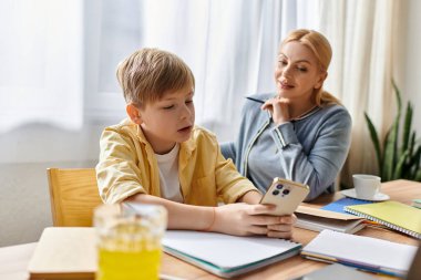 Bir anne, parlak bir masada seyyar bir cihazla iletişim kurarken oğluyla dikkatli bir şekilde temas kurar..