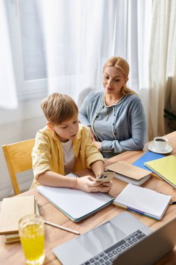 Annesi okul gereçleri masasında onunla uğraşırken bir çocuk telefonuyla oynuyor..