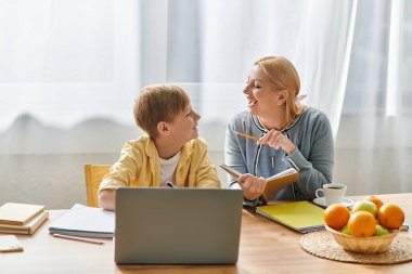 Bir anne oğluna ev ödevlerinde rehberlik eder, bilgi edinir ve parlak bir ortamda bağ kurar..