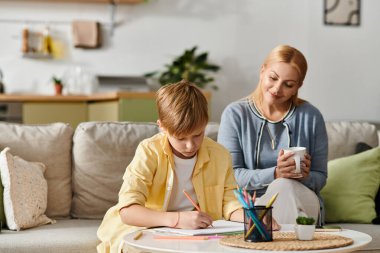 Bir kadın, oğlunun evindeki şık bir kahve masasında özenle çizim yapmasını izlemekten zevk alır..