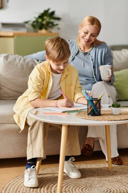 Bir anne oğlunun rahat bir oturma odası masasına renkli kalemlerle resim yapmasını izlemekten hoşlanır..