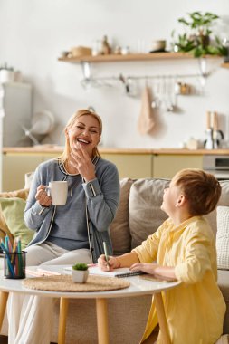 Bir anne sıcak bir içki yudumlarken oğlu yaratıcı aktivitelerle neşeyle meşgul oluyor..