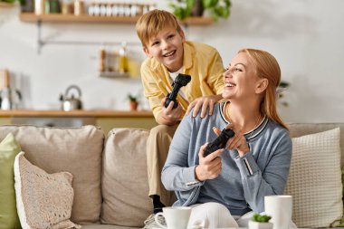 Neşeli bir anne ve oğlu modern oturma odalarında video oyunu oynayarak eğleniyorlar..