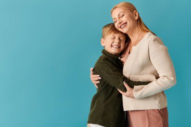 Bir anne ve oğlu sevgi dolu bir kucaklaşmayı paylaşıyor, parlak bir arka plana karşı sıcaklığını ve neşesini sergiliyor..