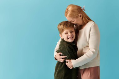 Bir anne eğilir, gülümseyen oğluyla sıcak bir kucaklaşmayı paylaşır, içten bir bağ kurar..