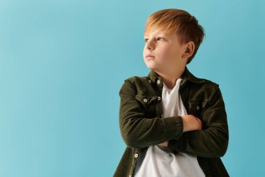 Kendine güvenen genç bir çocuk kollarını parlak mavi bir arkaplanda kavuşturur..