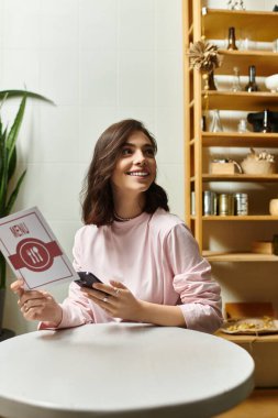 Güzel genç bir kadın şık bir kafede telefonuna bakarken gülümsüyor..