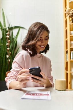 Modern bir kafedeki neşeli genç bir kadın telefonuyla konuşurken gülümsüyor..