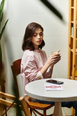 Modern bir kafede, genç ve güzel bir kadın kahvesini yudumluyor, düşünce ve sükunet içinde kayboluyor..