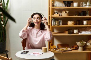Genç bir kadın şık bir kafede oturuyor, kulaklık takıyor ve içmekten zevk alırken gülümsüyor..