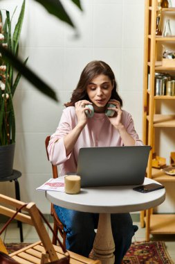Genç bir kadın, modern bir kafede rahat bir ortamın tadını çıkarırken laptopuyla birden fazla iş yapıyor..