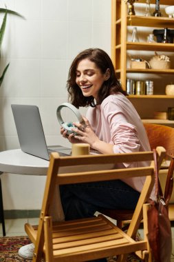 Güzel genç bir kadın rahat bir kafe atmosferinde dizüstü bilgisayarıyla çalışırken gülümsüyor..