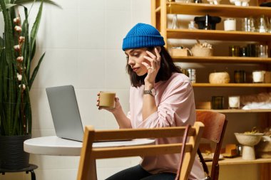 Genç bir kadın, rahat bir kafe ortamında dizüstü bilgisayarıyla çalışırken bir fincan içmekten hoşlanıyor..