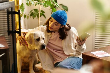 Genç bir kadın modaya uygun bir hayvan dostu kafede labradoruyla rahatlıyor, mutlu bir şekilde gülümsüyor..