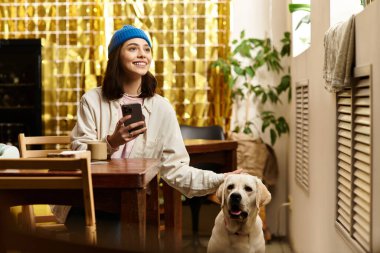 Genç bir kadın, modern bir kafede Labrador 'uyla gülüyor ve birlikte vakit geçiriyorlar..