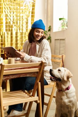 Modern bir kafede, genç bir kadın labradoruna gülümserken rahatlıyor ve kahvesini yudumluyor..