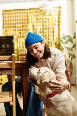 Genç bir kadın Labrador 'unu sıcacık bir kafe atmosferinde okşarken gülümsüyor..