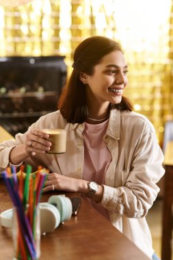 Genç bir kadın, sıcak bir kafede kahvesini yudumlarken, bir yandan da eğleniyor..