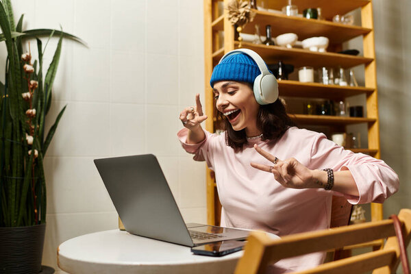 A beautiful young woman engages with her laptop, smiling joyfully in a vibrant cafe.