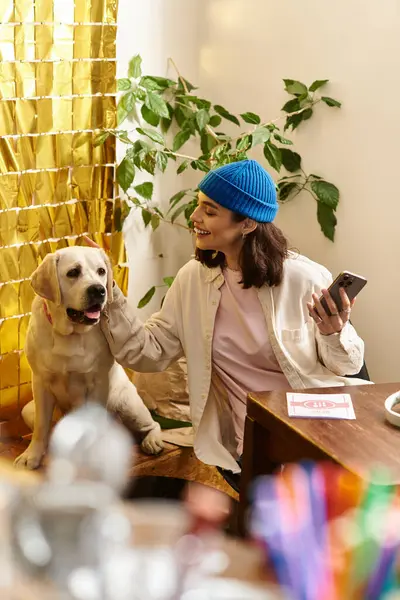 Genç bir kadın, Labrador 'uyla modern bir kafede oturmuş gününün tadını çıkarırken gülümsüyor..