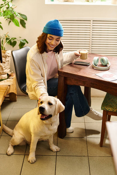 A young woman enjoys coffee while petting her labrador in a cozy cafe setting.