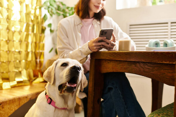 A pretty young woman relaxes with her labrador in a charming cafe, enjoying her coffee.
