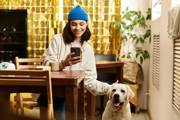 Genç ve güzel bir kadın bir kafede labradoruyla dinlenirken telefonuna gülümsüyor..