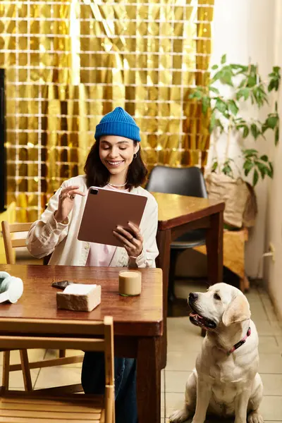 Genç bir kadın labradoruyla ahşap bir masada oturuyor. Evcil hayvan dostu bir kafede, gülümsemesini paylaşıyor..