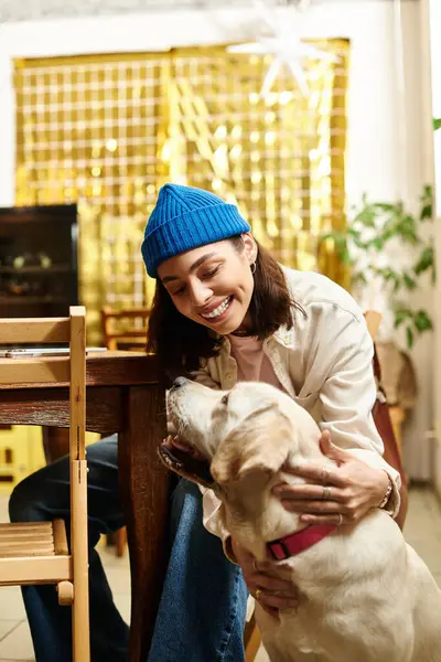Genç bir kadın Labrador 'unu sıcacık bir kafe atmosferinde okşarken gülümsüyor..