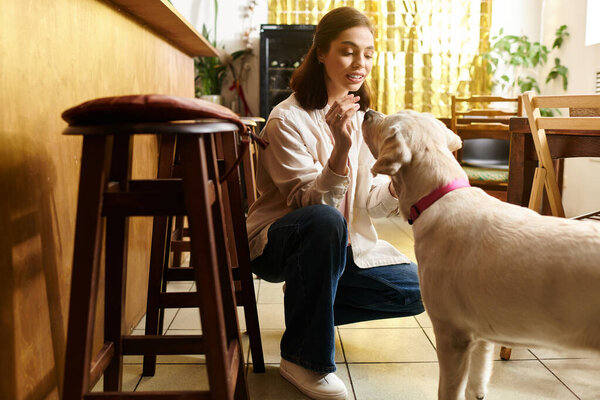 A young woman kneels in a cafe, happily interacting with her labrador as they share a moment.