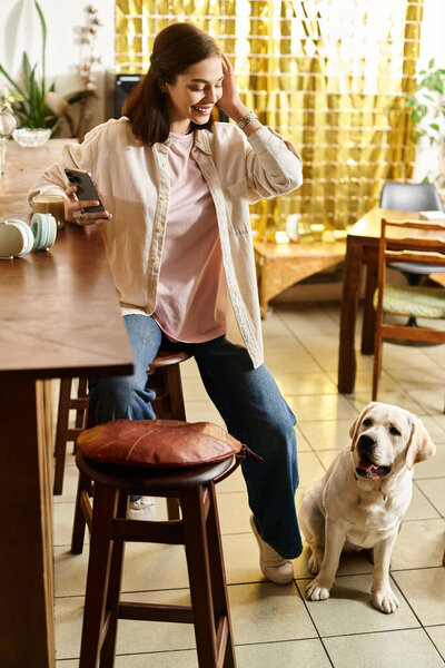 Pretty young woman laughs while seated with her labrador in a trendy pet-friendly cafe.
